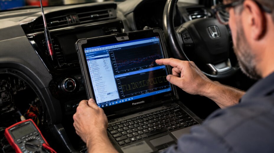 Technician using a laptop inside a car cabin to perform computerized blend door calibration and digital HVAC diagnostics, with disassembled panels and diagnostic tools visible.