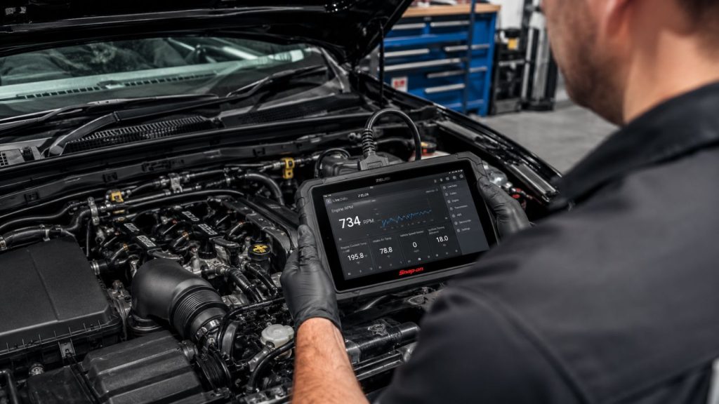 A professional mechanic at Ruben's Auto Care using a digital scan tool to diagnose engine idle speed on a vehicle with an open hood, identifying the root cause of stalls in I-10 West stop-and-go traffic.