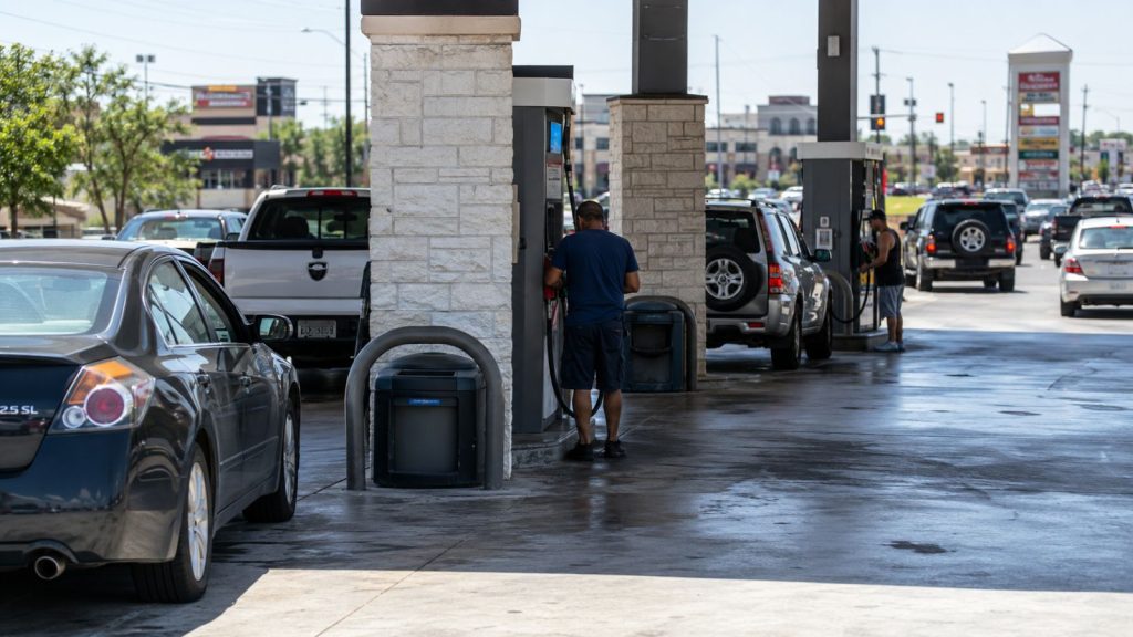 Heat waves shimmering off the asphalt at a busy San Antonio gas station near Loop 1604 and Bandera Road during a hot summer afternoon.