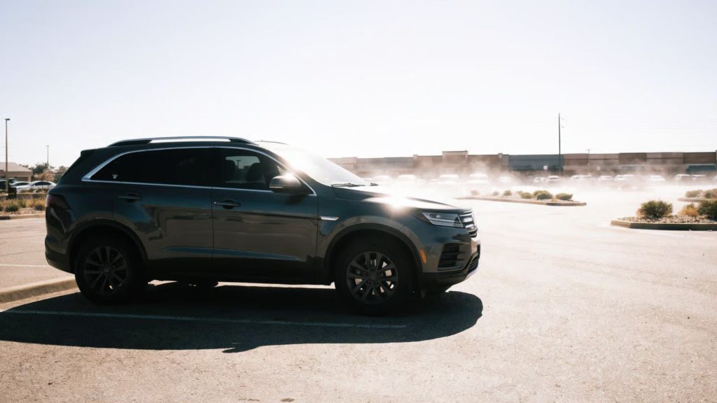 A modern SUV parked in a sun-drenched, hot retail parking lot during a summer afternoon, with visible heat haze shimmering above the asphalt.